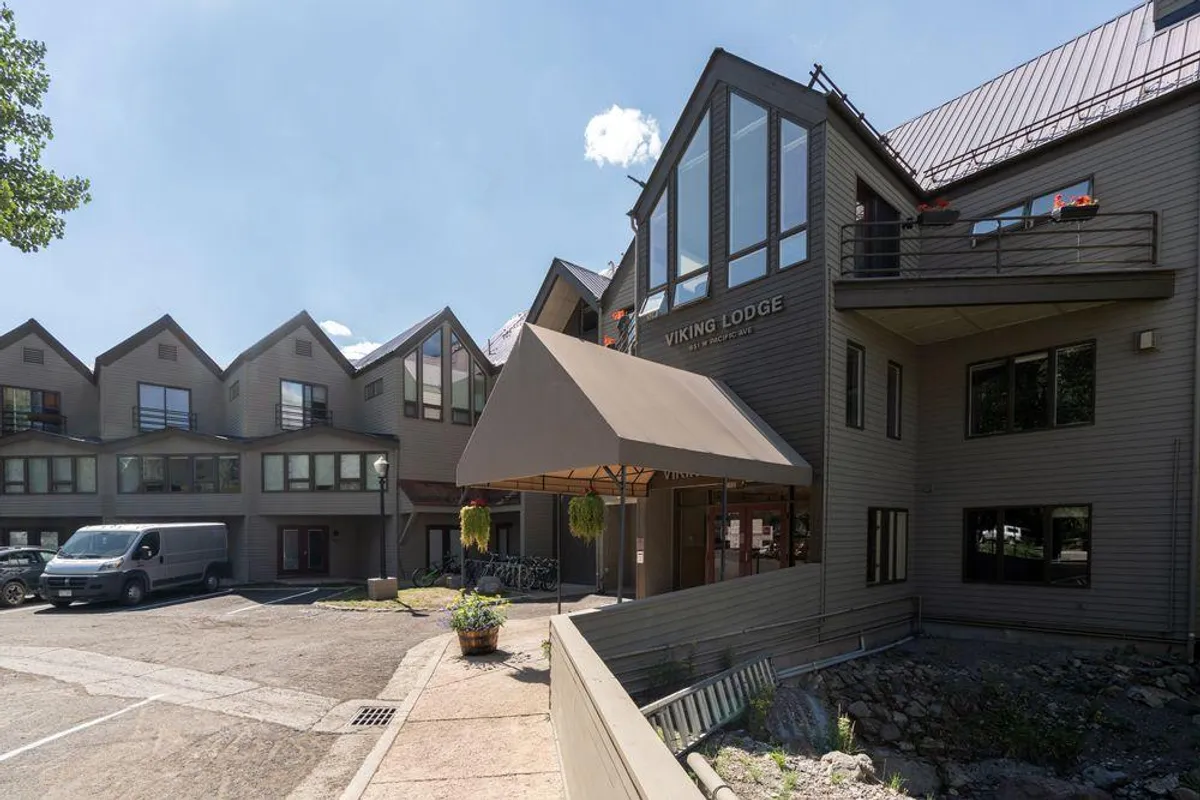 A bright, inviting exterior shot of the Viking Lodge entrance, featuring an awning, large windows, and welcoming landscaping. The signage clearly identifies the complex, and the landscaping conveys a sense of well-maintained, community-focused living.