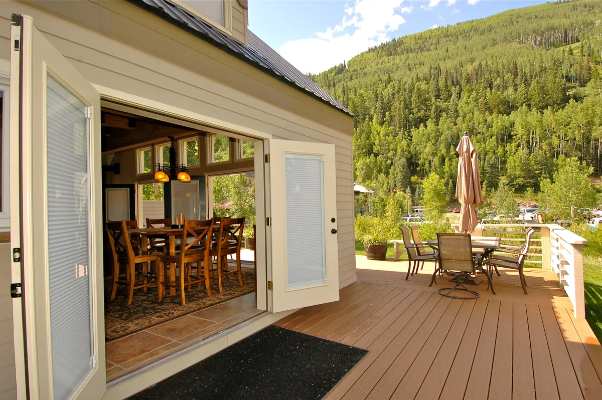 An inviting deck space with open doors leading from a dining area, outdoor seating arranged to maximize mountain views, and ample space for family gatherings. The deck seamlessly connects indoor and outdoor living.