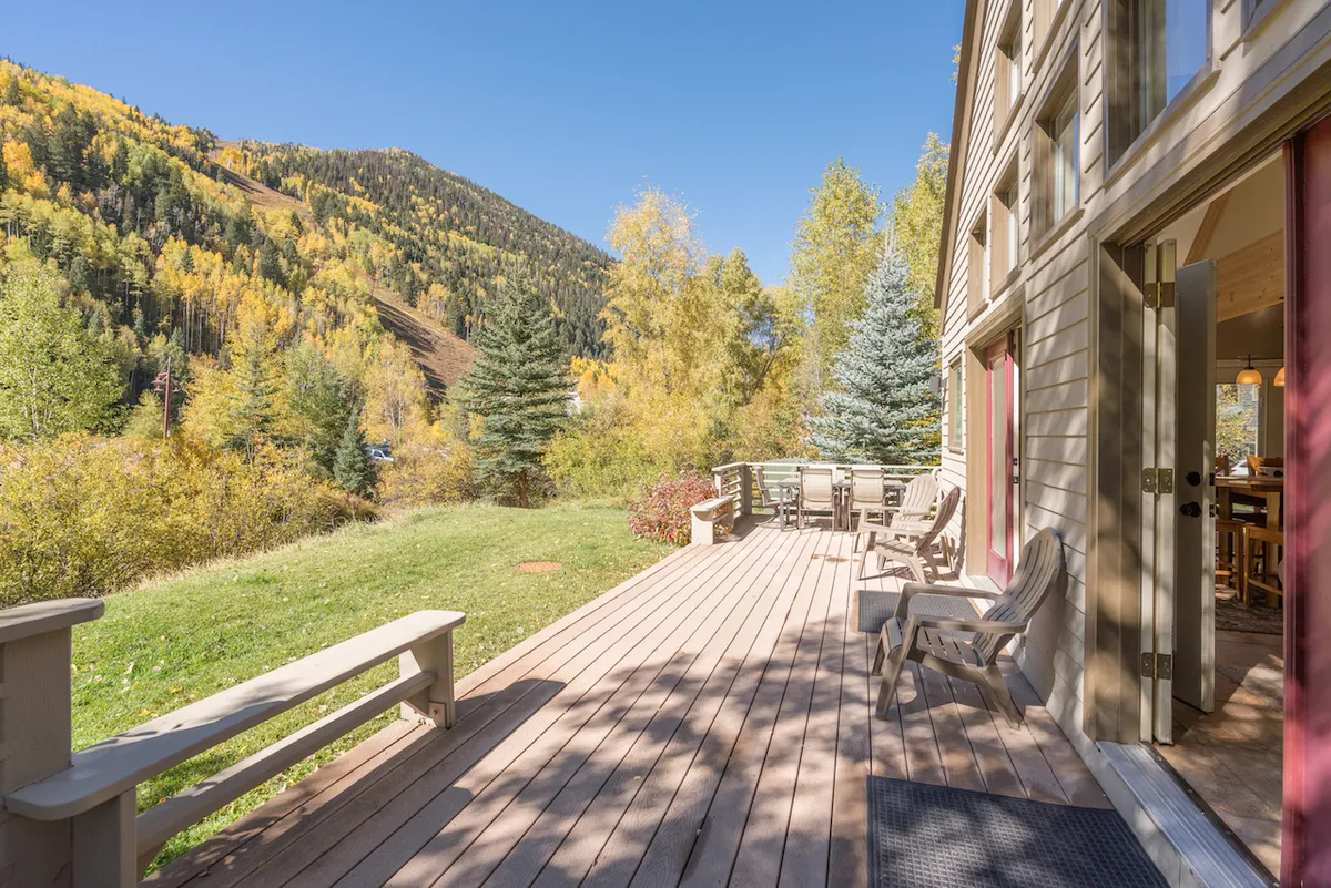 A wide deck area furnished with ample outdoor seating, set against a backdrop of trees and distant mountains. The setup hints at group gatherings and moments of relaxation, with the tranquil ambiance of the natural surroundings.