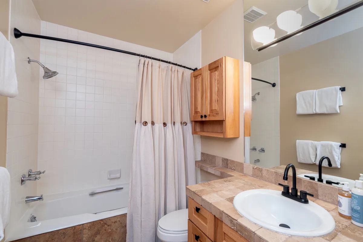 An interior view of a bathroom with a sleek bathtub, wooden cabinets, and a large mirror. The mood is tranquil and inviting, suggesting comfort and relaxation after active days.