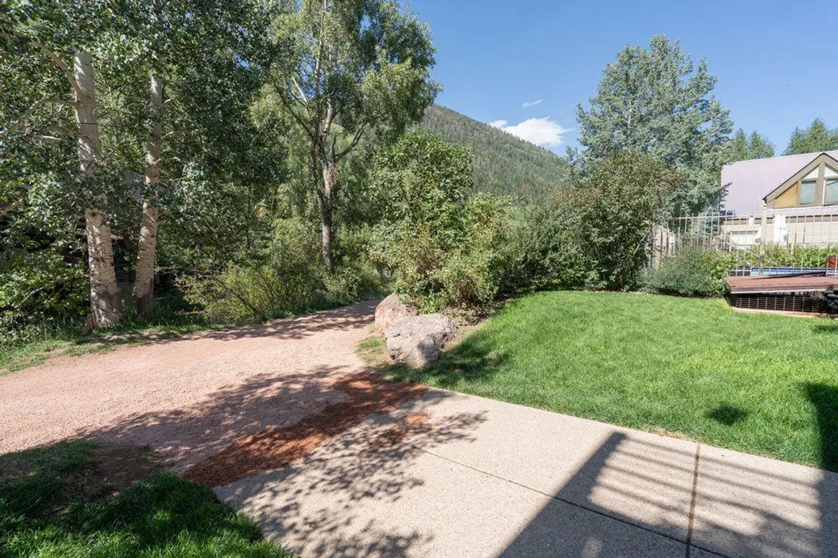 A peaceful exterior setting with a pathway winding through green grass and trees, set against a backdrop of mountains. The scene invites relaxation, nature walks, and summer outdoor enjoyment.